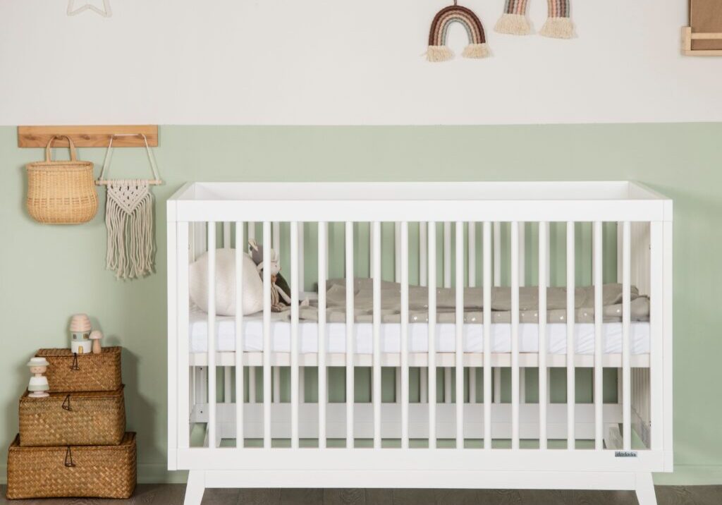 A baby crib with a cat sitting on it.