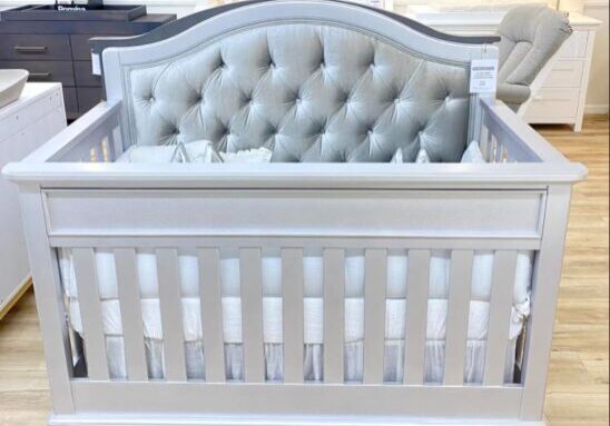 A baby crib with a tufted headboard and white trim.